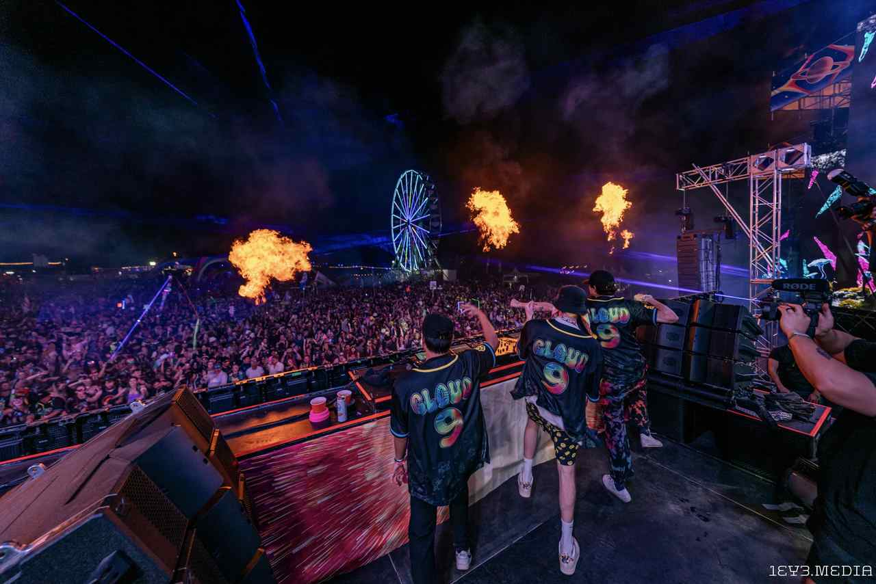 Festival stage with fire jets, lasers, and a Ferris wheel behind a huge crowd